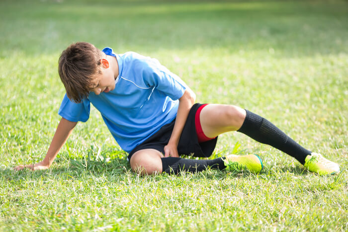 Child soccer player sitting on a grass field holding his leg in pain