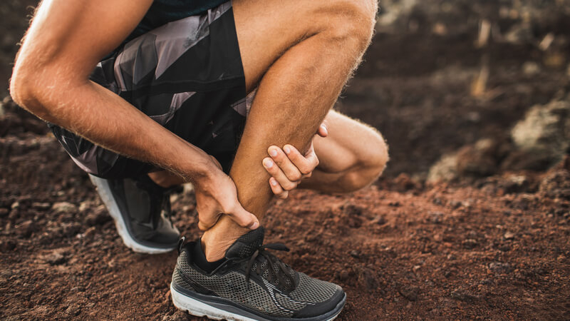 Man crouching down, holding Achilles heel with his hands