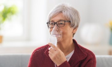 A woman doing a breathing treatment with a hand-held nebulizer