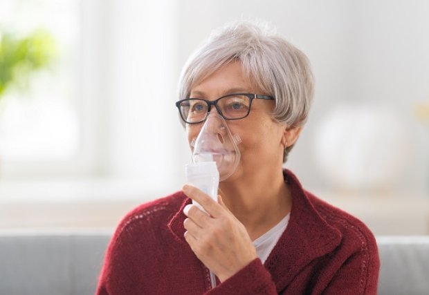 A woman doing a breathing treatment with a hand-held nebulizer